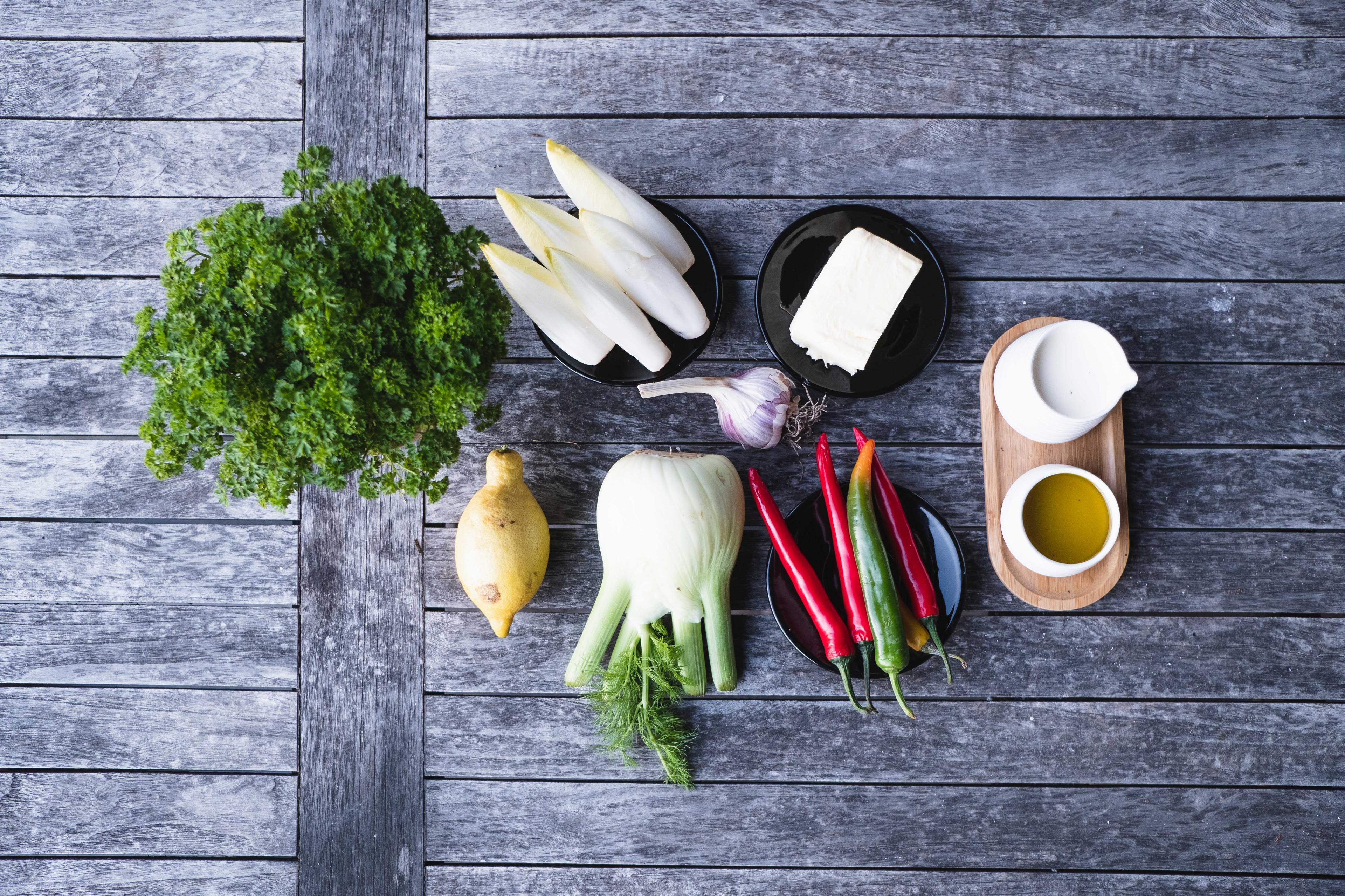 Petersilie, Zitrone, Öl, Butter, Sahne, Knoblauch, Chilies, Chicorée und Fenchel auf einer Tischplatte